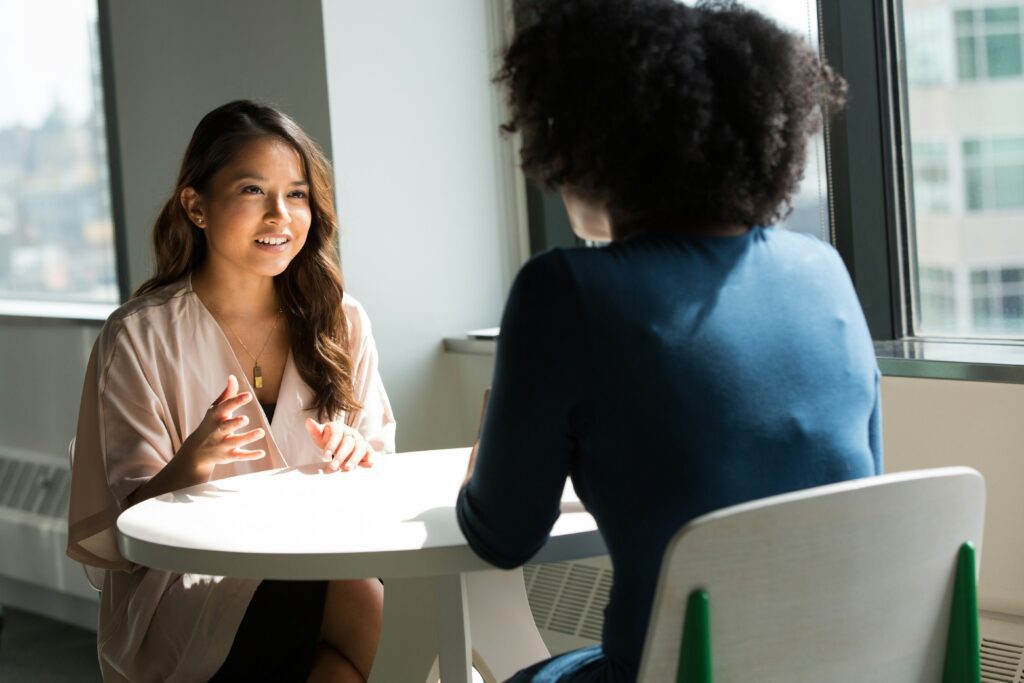 two women having a conversation at a table, the light from a window is lighting up one of the women's face.